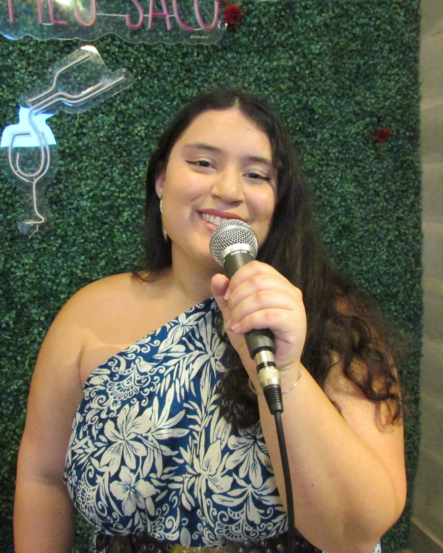Diana Blum se apresentando ao vivo, sorrindo com o microfone